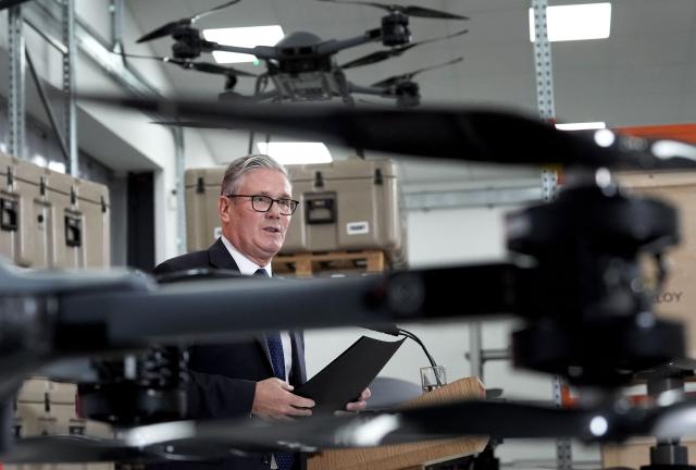 Britain's Prime Minister Keir Starmer stands beneath display of UAV drones, as he delivers a speech in Berkshire west of London, on June 30, 2026, following the publication of long-delayed Defence Investment Plan (DIP). Outgoing Prime Minister Keir Starmer announced on June 30, his long-delayed plan for funding Britain's future defence needs, with increased money for drones and autonomous systems. (Photo by Stefan Rousseau / POOL / AFP)