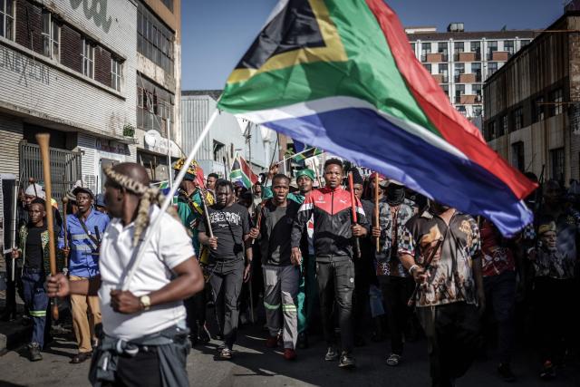 Protesters hold sticks and flags while chanting slogans as they march during a demonstration by the "March and March" and Operation Dudula movements marking an unofficial deadline set by citizen-led groups for undocumented foreign nationals to leave South Africa, in Johannesburg, on June 30, 2026. South African police deployed to head off unrest and protests on June 30, 2026, the unofficial deadline set by anti-immigrant groups for undocumented foreign nationals to leave that has already pushed thousands to flee.
Officers were out in force to prevent violence and looting by the xenophobic groups, while hundreds of foreign nationals took refuge in several cities, urgently seeking help to leave. (Photo by EMMANUEL CROSET / AFP)