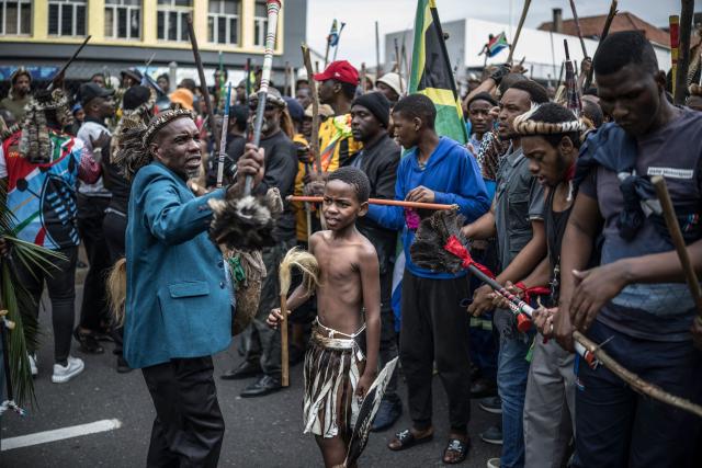 A young boy looks on as members of the Zulu regiment known as the “Amabutho” chant slogans while marching during a demonstration by the "March and March" movement marking an unofficial deadline set by citizen-led groups for undocumented foreign nationals to leave South Africa, in Durban, on June 30, 2026. Thousands of demonstrators massed across South African cities on June 30, 2026, venting anger at undocumented foreign nationals as police mounted a major operation to head off looting and xenophobic violence that has claimed four lives. 
The nationwide protests cap weeks of demonstrations called by a loose coalition of minor political parties and small citizen-led vigilante groups, which set an unofficial June 30 deadline for foreigners without residency papers to leave. (Photo by MARCO LONGARI / AFP)
