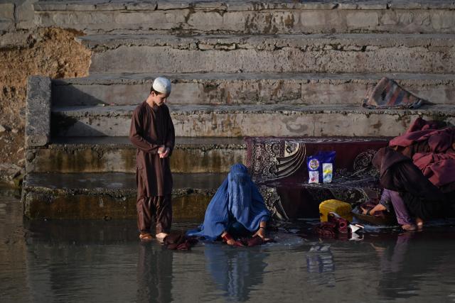 An Afghan burqa-clad woman washes carpets along a canal in Kandahar on June 30, 2026. (Photo by Sanaullah SEIAM / AFP)
