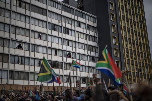 Residents observe from their apartments as members of the Zulu regiment known as the “Amabutho” chant slogans while marching during a demonstration by the "March and March" movement marking an unofficial deadline set by citizen-led groups for undocumented foreign nationals to leave South Africa, in Durban, on June 30, 2026. Thousands of demonstrators massed across South African cities on June 30, 2026, venting anger at undocumented foreign nationals as police mounted a major operation to head off looting and xenophobic violence that has claimed four lives. 
The nationwide protests cap weeks of demonstrations called by a loose coalition of minor political parties and small citizen-led vigilante groups, which set an unofficial June 30 deadline for foreigners without residency papers to leave. (Photo by MARCO LONGARI / AFP)