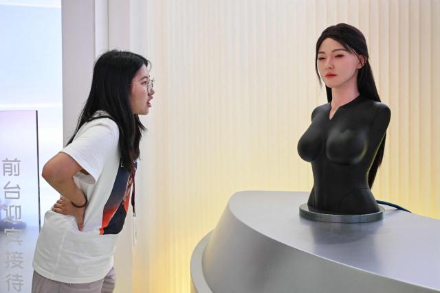 A woman (L) interacts with a humanoid robot (R) during the launch of the U1 humanoid robot produced by UWORLD, a brand under UBTECH Robotics, in Shenzhen, China's Guangdong province on June 30, 2026. Silicone skin, soothing voice: Chinese company UBTech unveiled unprecedented hyper-realistic human-looking androids equipped with artificial intelligence (AI) and presented as anti-loneliness remedies. (Photo by ADEK BERRY / AFP)