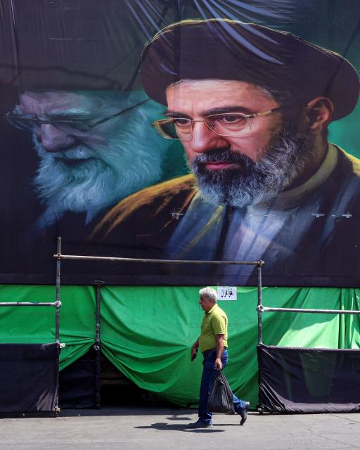 A man walks past a huge mourning banner depicting Iran's current supreme leader Mojtaba Khamenei and his late father Ali Khamenei, who was killed in a strike on the first day of the US-Israeli war against the Iran on February 28, set up along a road in Tehran on June 30, 2026 ahead of Ali Khamenei's funeral. Giant portraits of Ayatollah Ali Khamenei, Iran's late supreme leader killed in US-Israeli airstrikes, hung from Tehran's Grand Mosalla on June 30 as workers raced to prepare for his grandiose funeral ceremony. His public funeral, initially delayed at the height of the Middle East war, will begin on July 4 as Iran and the United States uphold a fragile ceasefire after signing a preliminary deal to end the conflict after more than three months. (Photo by AFP) / 