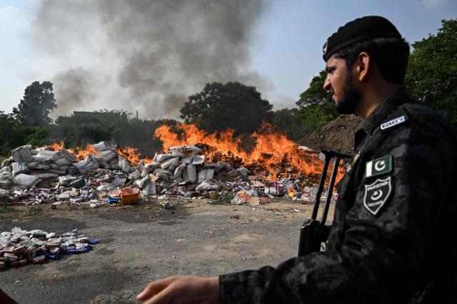 A Pakistan's customs personnel stands beside a burning pile of confiscated contraband goods during a destruction event in Islamabad on June 30, 2026. Pakistani customs authorities destroyed hundreds of illicit liquor bottles along with other contraband goods that had been seized after being smuggled into the country. (Photo by Aamir QURESHI / AFP)