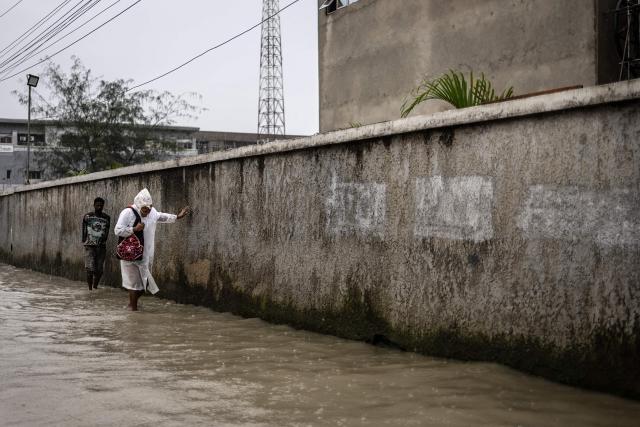 Pedestrians wade through a flooded street during rainfall in Lagos, on June 30, 2026. (Photo by OLYMPIA DE MAISMONT / AFP)