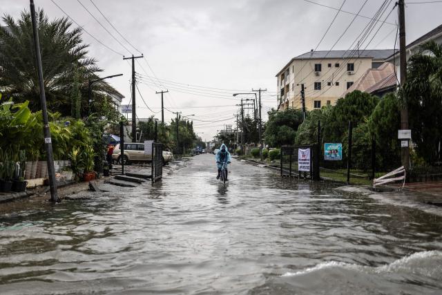 TOPSHOT - A man wearing a raincoat cycles along a flooded street during rainfall in Lagos, on June 30, 2026. (Photo by OLYMPIA DE MAISMONT / AFP)