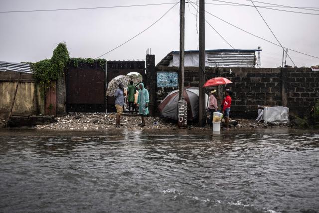 Residents stand on the side of a flooded street during rainfall in Lagos, on June 30, 2026. (Photo by OLYMPIA DE MAISMONT / AFP)