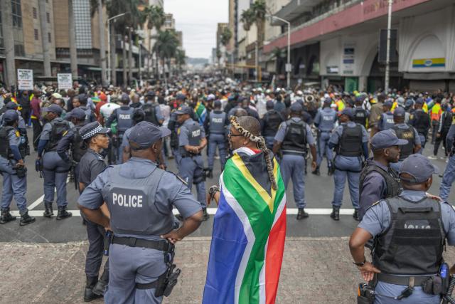 Members of the South African Police Service (SAPS) monitor the crowd during a demonstration by the "March and March" movement marking an unofficial deadline set by citizen-led groups for undocumented foreign nationals to leave South Africa, in Durban, on June 30, 2026. Thousands of demonstrators massed across South African cities on June 30, 2026, venting anger at undocumented foreign nationals as police mounted a major operation to head off looting and xenophobic violence that has claimed four lives. 
The nationwide protests cap weeks of demonstrations called by a loose coalition of minor political parties and small citizen-led vigilante groups, which set an unofficial June 30 deadline for foreigners without residency papers to leave. (Photo by RAJESH JANTILAL / AFP)