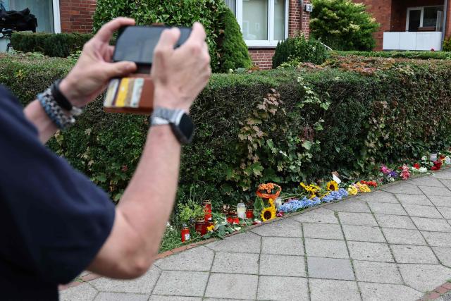 A man takes a photo of the flowers and candles left at a makeshift memorial at the scene where six people were killed in a shooting the day before in Stade, northern Germany, a city some 50 kilometres west of Hamburg, on June 30, 2026. The suspected shooter who killed six people at a German youth welfare centre on Monday was in a custody dispute over his three-month-old daughter, police said. The victims of the shooting -- four women and two men -- were youth welfare employees, a police official told a press conference. The girl and her mother were in the office at the time of the shooting but were not harmed. (Photo by Ibrahim OT / AFP)