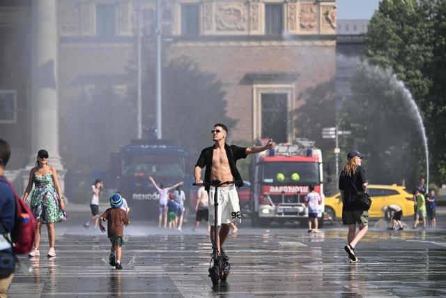 TOPSHOT - Police use water cannon to cool down people in Budapest's Heroes' Square during an extreme heat wave on June 30, 2026. Police and fire department vehicles sprayed water in the afternoon to relieve the high temperatures. The cooling initiative was well received by visitors, while a third-degree heat alert remains in effect nationwide and century-old heat (Photo by Attila KISBENEDEK / AFP)