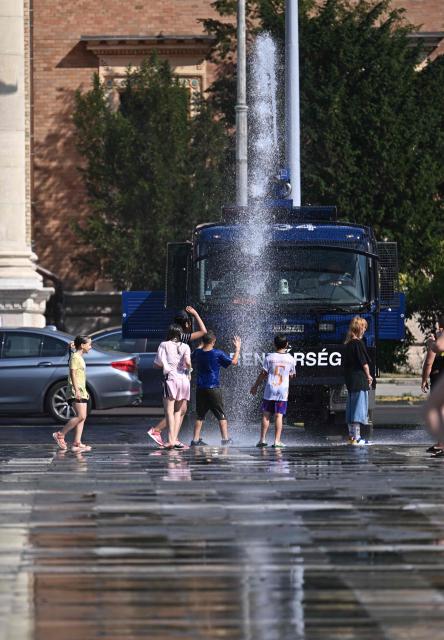 Police use water cannon to cool down people in Budapest's Heroes' Square during an extreme heat wave on June 30, 2026. Police and fire department vehicles sprayed water in the afternoon to relieve the high temperatures. The cooling initiative was well received by visitors, while a third-degree heat alert remains in effect nationwide and century-old heat (Photo by Attila KISBENEDEK / AFP)