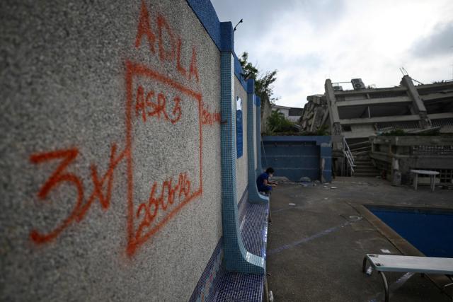 Orange spray-painted rescue team markings are seen on a wall next to a damaged swimming pool and collapsed residential structures in a complex in Caraballeda, La Guaira state, Venezuela, on June 30, 2026, following twin earthquakes that struck the coastal region. Tens of thousands of people desperately sought food and shelter in Venezuela on June 30 after the two earthquakes killed nearly 2,000, but rescue teams managed to pull a 3-year-old boy alive from the rubble six days after the shocks. (Photo by Juan BARRETO / AFP)