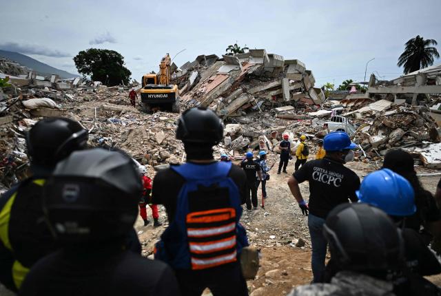 Volunteers and paramedics stand still as rescuers carry out sound tests in search of survivors following the June 24 twin earthquakes, in Caraballeda, La Guaira state, Venezuela, on June 30, 2026. Tens of thousands of people urgently need food and shelter in Venezuela due to the devastation from two huge earthquakes that killed more than 1,700 and injured 5,000, the UN said on June 30, 2026, as doctors warned of potential outbreaks of disease. (Photo by Juan BARRETO / AFP)