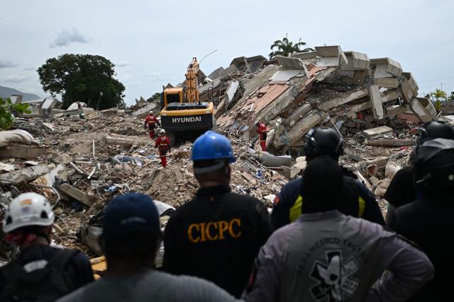 Volunteers and paramedics stand still as rescuers carry out sound tests in search of survivors following the June 24 twin earthquakes, in Caraballeda, La Guaira state, Venezuela, on June 30, 2026. Tens of thousands of people urgently need food and shelter in Venezuela due to the devastation from two huge earthquakes that killed more than 1,700 and injured 5,000, the UN said on June 30, 2026, as doctors warned of potential outbreaks of disease. (Photo by Juan BARRETO / AFP)
