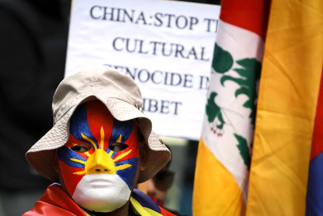A member of the Australian Tibetan community wears a mask as he stands next to fellow protesters holding placards and flags during a protest in Sydney on July 1, 2026. (Photo by DAVID GRAY / AFP)