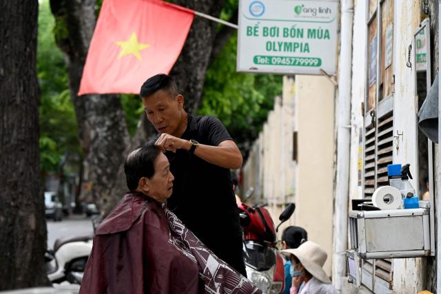 A roadside barber cuts the hair of a customer in Hanoi on July 1, 2026. (Photo by Nhac NGUYEN / AFP)