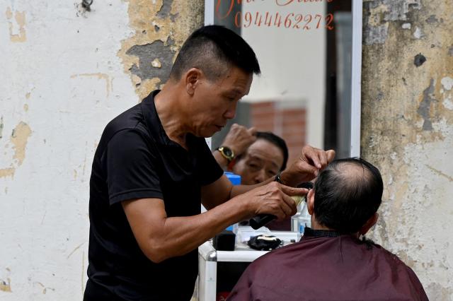 A roadside barber cuts the hair of a customer in Hanoi on July 1, 2026. (Photo by Nhac NGUYEN / AFP)