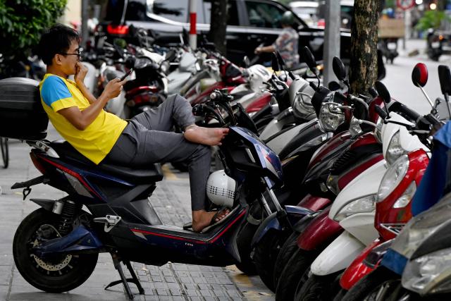 A man uses his phone while sitting on an electric scooter on a sidewalk in Hanoi on July 1, 2026. (Photo by Nhac NGUYEN / AFP)