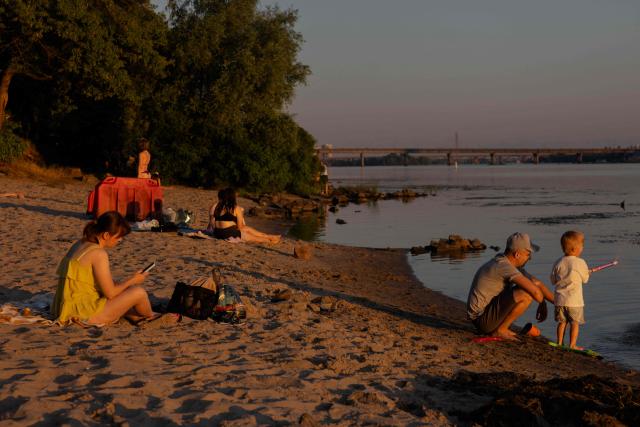 People sit on the beach at sunset near the Dnipro River during a hot summer’s day in Kyiv on June 30, 2026, amid the Russian invasion of Ukraine. (Photo by Tetiana DZHAFAROVA / AFP)