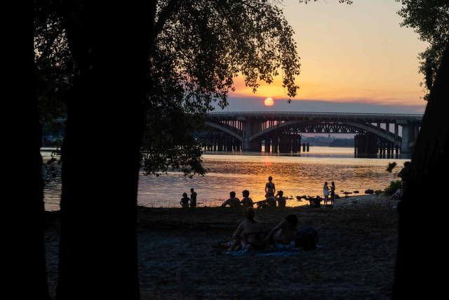 People sit on the beach at sunset near the Dnipro River during a hot summer’s day in Kyiv on June 30, 2026, amid the Russian invasion of Ukraine. (Photo by Tetiana DZHAFAROVA / AFP)