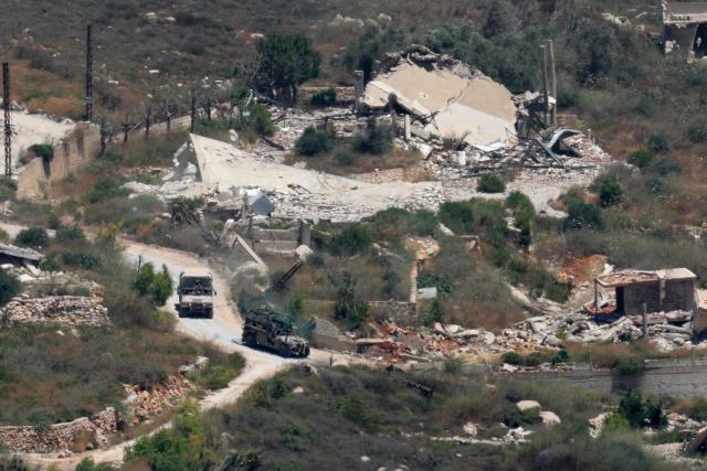 This picture taken from a position in the Upper Galilee in northern Israel shows Israeli military vehicles driving past houses destroyed in Israeli strikes in the southern Lebanese village near the Israel-Lebanon border, on July 1, 2026. Israel's defence minister said on July 1 that Israeli forces would remain in self-proclaimed "security zones" established in Lebanon, Syria and Gaza, without any timeline for withdrawal. (Photo by Jack GUEZ / AFP) / 