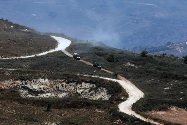 This picture taken from a position in the Upper Galilee in northern Israel shows Israeli military vehicles driving past houses destroyed in Israeli strikes in the southern Lebanese village near the Israel-Lebanon border, on July 1, 2026. Israel's defence minister said on July 1 that Israeli forces would remain in self-proclaimed "security zones" established in Lebanon, Syria and Gaza, without any timeline for withdrawal. (Photo by Jack GUEZ / AFP) / 