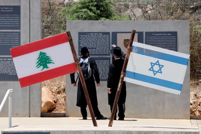 Ultra-Orthodox Jewish men stand beside Israeli and Lebanese flags at a memorial site on the border with Lebanon in northern Israel, on July 1, 2026. Israel's defence minister said on July 1 that Israeli forces would remain in self-proclaimed "security zones" established in Lebanon, Syria and Gaza, without any timeline for withdrawal. (Photo by Jack GUEZ / AFP) / 