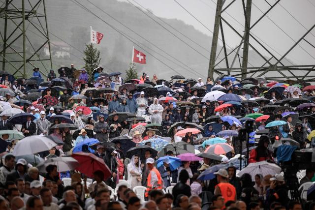 Worshippers stand under a strom during the schismatic consecration of bishops by the traditionalist Catholic Society of Saint Pius X (SSPX) in Econe, western Switzerland, on July 1, 2026. The Society of Saint Pius X consecrated four new bishops on July 1, 2026, in defiance of Pope Leo XIV, who pleaded with the ultra-traditionalist breakaway group to turn back from what he called a "schismatic act" with Rome. (Photo by Fabrice COFFRINI / AFP)