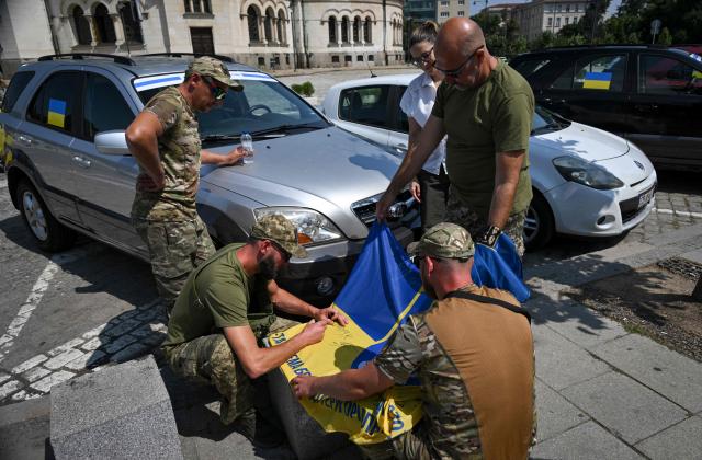 Soldiers of the Ukrainian army write messages on an Ukrainian flag during a ceremony to hand over 17 off-road vehicles donated from Bulgarians and Russians, living in Bulgaria, in front of Alexander Nevsky Cathedral in Sofia on July 1, 2026. (Photo by Nikolay DOYCHINOV / AFP)