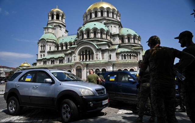 Soldiers of the Ukrainian army stand next to donated cars during a ceremony to hand over 17 off-road vehicles donated from Bulgarians and Russians, living in Bulgaria, in front of Alexander Nevsky Cathedral in Sofia on July 11, 2026. (Photo by Nikolay DOYCHINOV / AFP)
