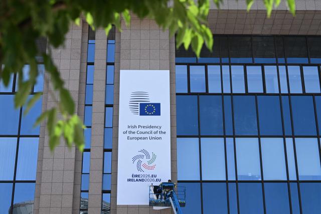 Workers on a platform put up the new poster announcing the start of the Irish presidency of the EU for the next six months on the facade of the European Council in Brussels, on July 1, 2026. (Photo by Nicolas TUCAT / AFP)