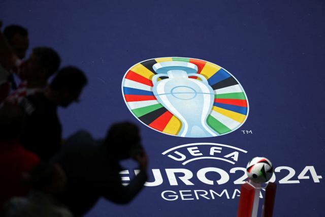 (FILES) In this file photo taken on June 19, 2024 supporters are seen near the official logo and ball of the Euro before the start of the UEFA Euro 2024 Group B football match between Croatia and Albania at the Volksparkstadion in Hamburg. Investigators raided Germany's football association headquarters and other locations across the country on July 1, 2026 as part of an investigation into corruption linked to the Euro 2024 tournament. The DFB confirmed that its headquarters in Frankfurt had been targeted. The case involves allegations that employees of German host cities were illegally invited to Euro matches and received tickets on favourable terms from the organisers, police and prosecutors said. (Photo by Ronny HARTMANN / AFP)