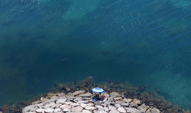 (FILES) This aerial photograph shows a man sunbathing on rocks in front of the sea in Durres, western Albania, on June 29, 2026. According to the European Union's Copernicus Marine Service, the world's oceans just experienced their hottest June on record, global average sea surface temperatures in June were 20.98C, beating the previous records of 2023 and 2024, and could set fresh highs in the months ahead as El Nino and climate change drive temperatures even higher, scientists said on July 01, 2026. (Photo by Adnan Beci / AFP)