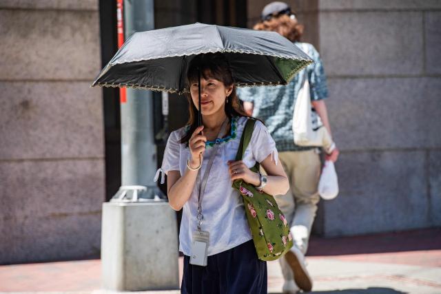 A person walks with an umbrella during a heat wave in Boston, Massachusetts on July 1, 2026. Tens of millions of Americans sweltered under furnace-like temperatures this week as central and eastern cities hunkered down for a heat wave set to last through the July 4 holiday weekend. Dozens of local temperature records could be broken, the National Weather Service (NWS) warned, with temperatures in many places to surpass 100 degrees Fahrenheit (38 degrees Celsius) and high humidity pushing the heat index as high as 115 degrees. (Photo by Joseph Prezioso / AFP)