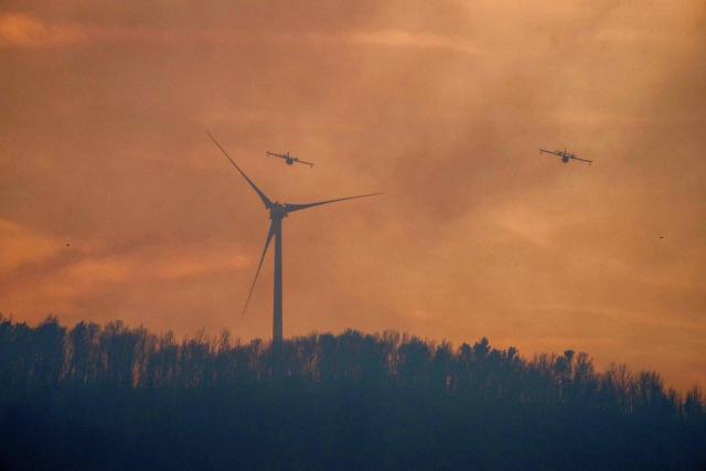 This photograph shows French civil security aircrafts flying over a wildfire, next to a wind turbine, in Pouzols-Minervois, southwestern of France, on July 1, 2026. (Photo by Idriss Bigou-Gilles / AFP)