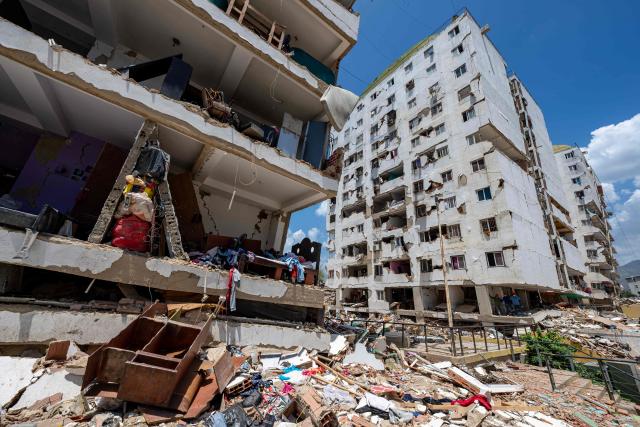 This photograph shows a damaged building with debris scattered in the foreground in Playa Grande neighborhood, La Guaira state, Venezuela, on July 1, 2026, following the June 24 twin earthquakes. Tens of thousands of people urgently need food and shelter in Venezuela due to the devastation from two huge earthquakes that killed more than 1,700 and injured 5,000, the UN said on June 30, 2026, as doctors warned of potential outbreaks of disease. (Photo by Miguel MEDINA / POOL / AFP)