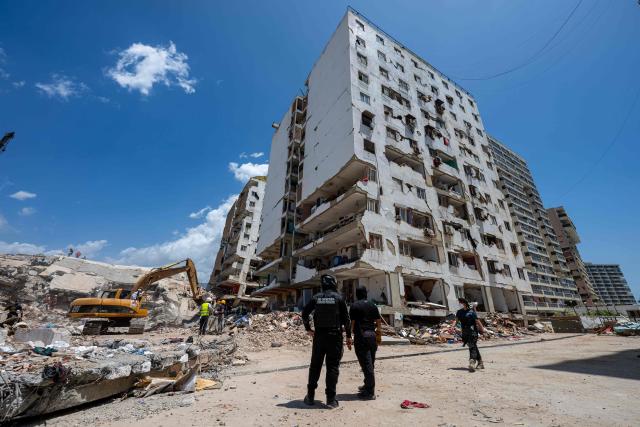 Rescue workers stand near an excavator amid debris as damaged residential buildings are seen in Playa Grande neighbourhood, La Guaira state, Venezuela, on July 1, 2026, following the June 24 twin earthquakes. Tens of thousands of people urgently need food and shelter in Venezuela due to the devastation from two huge earthquakes that killed more than 1,700 and injured 5,000, the UN said on June 30, 2026, as doctors warned of potential outbreaks of disease. (Photo by Miguel MEDINA / POOL / AFP)