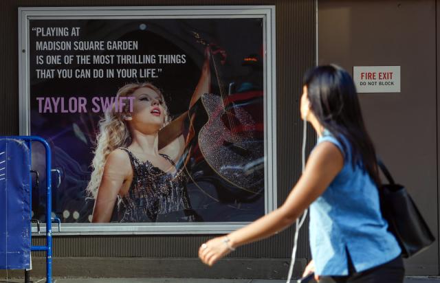 A person walks by a poster featuring an image and quote from US singer-songwriter Taylor Swift outside Madison Square Garden in New York on July 1, 2026. Increasing signs point to a mega-bash for the A-list celebrity couple Taylor Swift and Travis Kelce at Madison Square Garden this week. Rumors have run rampant for weeks that the 36-year-old pop superstar and the three-time NFL Super Bowl winner, both 36, could wed at the storied sports arena, home to the New York Knicks, the newly crowned NBA champions. (Photo by kena betancur / AFP)