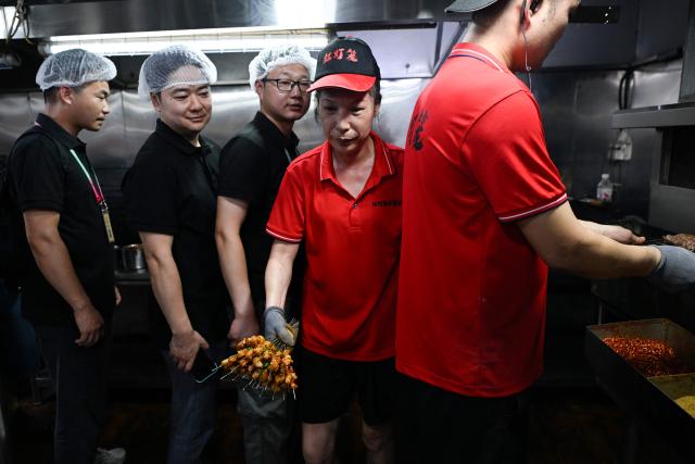 This picture taken on June 15, 2026 shows a group of trainees (L) visiting a barbecue restaurant in Yueyang, in southern China's Hunan province. Hunched over sizzling grills and shrouded in smoke drifting from white-hot charcoal, dozens of trainees at the Yueyang Barbecue Academy in southern China roast skewer after skewer of succulent beef tendon to perfect the fragrant, spicy taste of their homework. (Photo by WANG Zhao / AFP) / TO GO WITH: China-culture-food-bbq, by Sam DAVIES