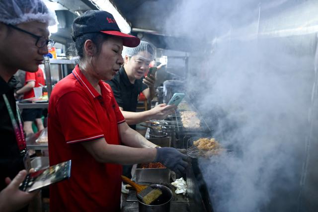 This picture taken on June 15, 2026 shows a barbecue chef (C) demonstrating techniques to trainees at a barbecue restaurant in Yueyang, in southern China's Hunan province. Hunched over sizzling grills and shrouded in smoke drifting from white-hot charcoal, dozens of trainees at the Yueyang Barbecue Academy in southern China roast skewer after skewer of succulent beef tendon to perfect the fragrant, spicy taste of their homework. (Photo by WANG Zhao / AFP) / TO GO WITH: China-culture-food-bbq, by Sam DAVIES