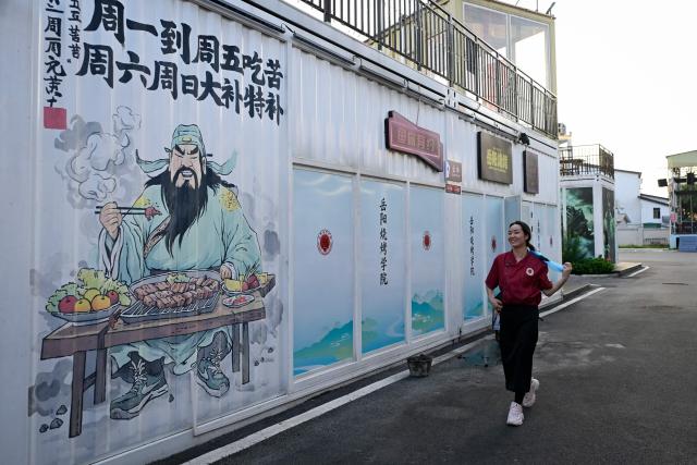 This picture taken on June 15, 2026 shows a trainee walking at Barbecue Academy during a day’s training in Yueyang, in southern China's Hunan province. Hunched over sizzling grills and shrouded in smoke drifting from white-hot charcoal, dozens of trainees at the Yueyang Barbecue Academy in southern China roast skewer after skewer of succulent beef tendon to perfect the fragrant, spicy taste of their homework. (Photo by WANG Zhao / AFP) / TO GO WITH: China-culture-food-bbq, by Sam DAVIES
