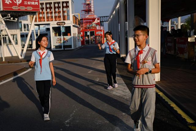 This picture taken on June 15, 2026 shows a group of pupils, who live near the Yueyang Barbecue Academy tasting BBQ, tasting skewers cooked by trainees at the Yueyang Barbecue Academy in Yueyang, in southern China's Hunan province. Hunched over sizzling grills and shrouded in smoke drifting from white-hot charcoal, dozens of trainees at the Yueyang Barbecue Academy in southern China roast skewer after skewer of succulent beef tendon to perfect the fragrant, spicy taste of their homework. (Photo by WANG Zhao / AFP) / TO GO WITH: China-culture-food-bbq, by Sam DAVIES