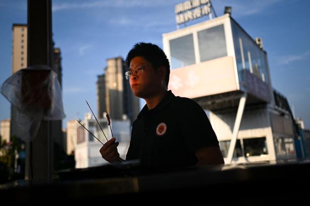 This picture taken on June 15, 2026 shows a trainee tasting BBQ skewers made by himself at the Yueyang Barbecue Academy in Yueyang, in southern China's Hunan province. Hunched over sizzling grills and shrouded in smoke drifting from white-hot charcoal, dozens of trainees at the Yueyang Barbecue Academy in southern China roast skewer after skewer of succulent beef tendon to perfect the fragrant, spicy taste of their homework. (Photo by WANG Zhao / AFP) / TO GO WITH: China-culture-food-bbq, by Sam DAVIES