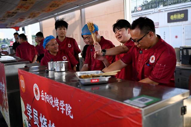 This picture taken on June 15, 2026 shows a trainee reacting as he looks at skewers made by himself during practical session at the Yueyang Barbecue Academy in Yueyang, in southern China's Hunan province. Hunched over sizzling grills and shrouded in smoke drifting from white-hot charcoal, dozens of trainees at the Yueyang Barbecue Academy in southern China roast skewer after skewer of succulent beef tendon to perfect the fragrant, spicy taste of their homework. (Photo by WANG Zhao / AFP) / TO GO WITH: China-culture-food-bbq, by Sam DAVIES