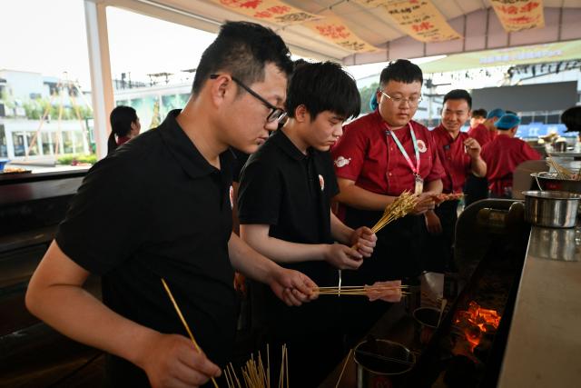 This picture taken on June 15, 2026 shows trainees taking part in BBQ practical session at the Yueyang Barbecue Academy in Yueyang, in southern China's Hunan province. Hunched over sizzling grills and shrouded in smoke drifting from white-hot charcoal, dozens of trainees at the Yueyang Barbecue Academy in southern China roast skewer after skewer of succulent beef tendon to perfect the fragrant, spicy taste of their homework. (Photo by WANG Zhao / AFP) / TO GO WITH: China-culture-food-bbq, by Sam DAVIES