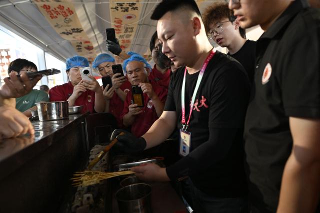 This picture taken on June 15, 2026 shows a group of trainees using mobile phones to record during a practical session at the Yueyang Barbecue Academy in Yueyang, in southern China's Hunan province. Hunched over sizzling grills and shrouded in smoke drifting from white-hot charcoal, dozens of trainees at the Yueyang Barbecue Academy in southern China roast skewer after skewer of succulent beef tendon to perfect the fragrant, spicy taste of their homework. (Photo by WANG Zhao / AFP) / TO GO WITH: China-culture-food-bbq, by Sam DAVIES