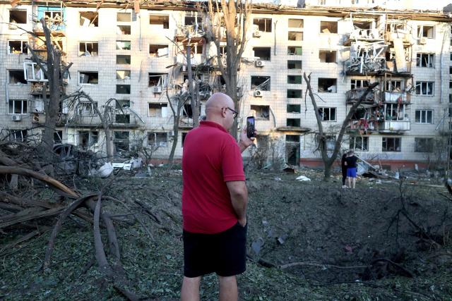 A man takes pictures of a crater next to a damaged residential building following missile strikes on the Ukrainian capital of Kyiv on July 2, 2026, amid the Russian invasion of Ukraine. Russian missile and drone strikes rocked Kyiv early on Thursday, setting off fires and wounding at least five people, after President Volodymyr Zelensky warned that Moscow was preparing a "massive attack". (Photo by Serhii Okunev / AFP)