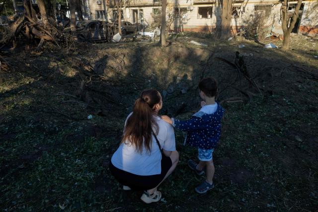 A woman and a child stand near a crater next to a residential building damaged following a Russian air attack on the Ukrainian capital of Kyiv on July 2, 2026, amid the Russian invasion in Ukraine. Russian missile and drone strikes rocked Kyiv early on July 2, killing at least eight people and wounding dozens, after President Volodymyr Zelensky warned that Moscow was preparing a "massive attack". (Photo by Tetiana DZHAFAROVA / AFP)