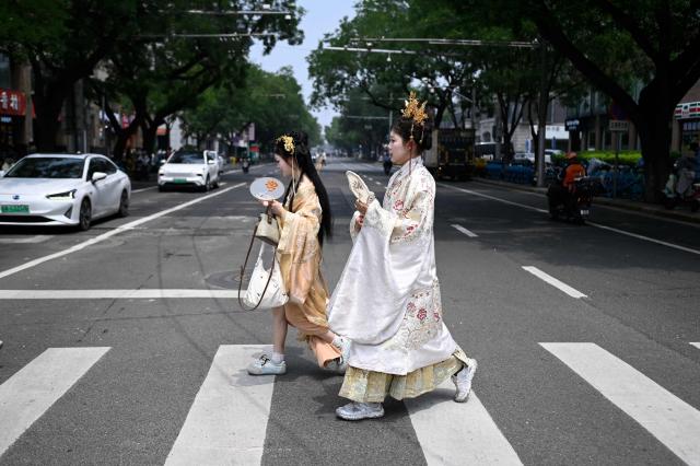 Two women wearing traditional clothes cross a street on a hot day in Beijing on July 2, 2026. (Photo by WANG Zhao / AFP)