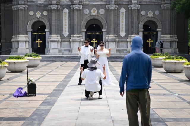 A photographer guides a couple to pose for their wedding photos in front of a church in Beijing on July 2, 2026. (Photo by WANG Zhao / AFP)